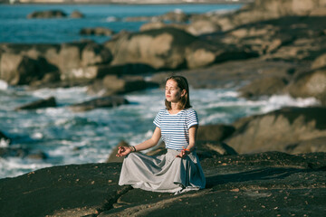 A yoga woman meditates in the lotus position on the ocean coast at day.