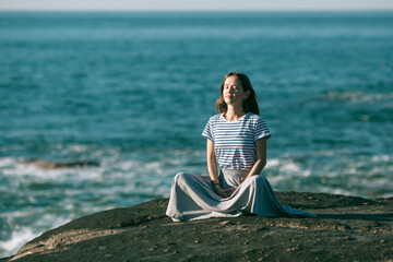 A girl meditating on the sea beach during a wonderful sunrise. Yoga and fitness.