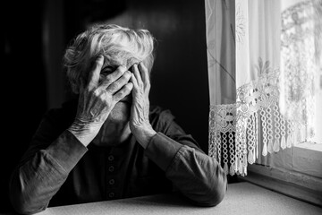 An old woman covers her face with wrinkled hands. Black and white photo.