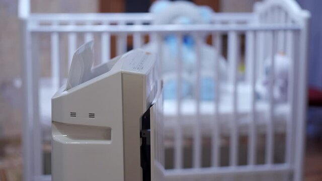 Modern air purifier humidifier in bedroom, working humidifier in front of baby cot creating a more comfortable environment at home. Climatic device