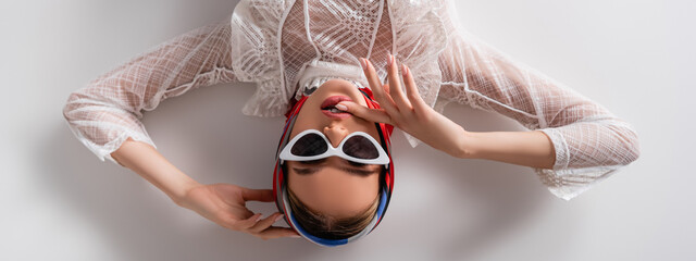top view of trendy woman in headscarf and sunglasses lying while looking at camera on white, banner