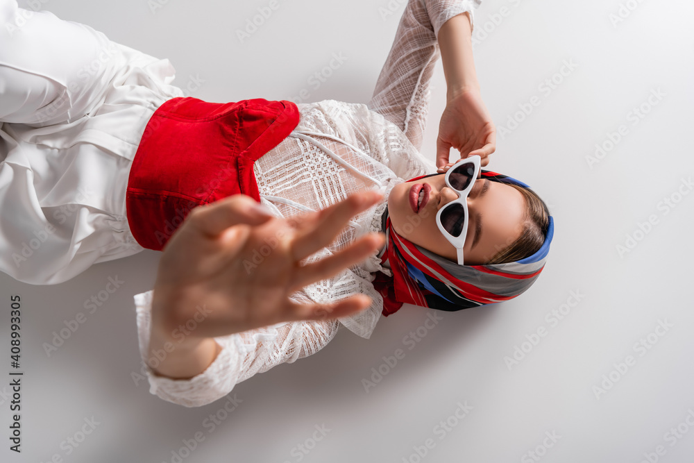 Sticker top view of trendy woman in headscarf and sunglasses lying with outstretched hand on white