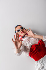 high angle view of trendy woman in headscarf and sunglasses lying while gesturing on white