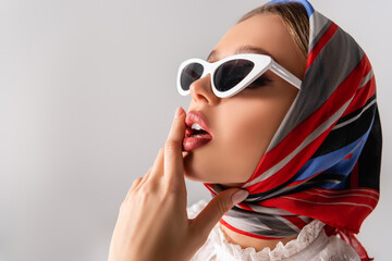 young and sensual woman in headscarf and sunglasses touching lips isolated on white - obrazy, fototapety, plakaty