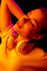 Party. Caucasian woman's portrait on black studio background in pink-orange neon light. Beautiful female model with headphones. Concept of human emotions, facial expression, sales, ad, fashion.