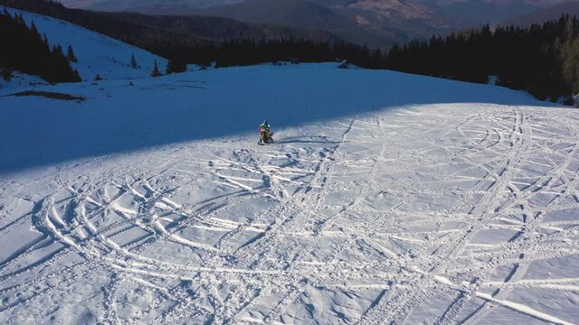 Snowbike riders in mountain valley in beautiful snow powder. Aerial video. Snowdirt bike with splashes and trail. Snowmobile winter sport riding