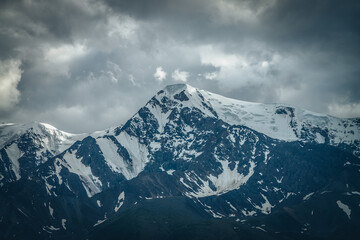 Dramatic mountains landscape with big snowy mountain ridge under cloudy sky. Dark atmospheric highland scenery with high mountain range in overcast weather. Awesome big mountains under gray clouds.