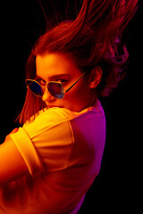 Style. Caucasian woman's portrait on black studio background in orange-pink neon light. Beautiful female model with blowing hairs out. Concept of human emotions, facial expression, sales, ad, fashion.