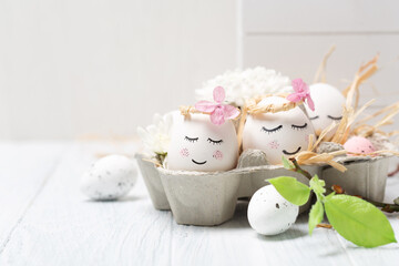 Easter holiday concept with cute handmade white eggs, tree branches, quail feathers and spring flowers on white wooden background.