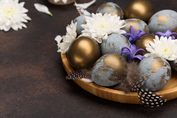 Easter Decoration with gray blue golden eggs, quail feathers, white flowers on dark wooden background. Selective focus, copy space.