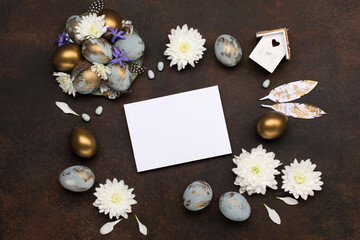 Easter Decoration with gray blue golden eggs, quail feathers, white flowers on dark wooden background. Copy space, top view.