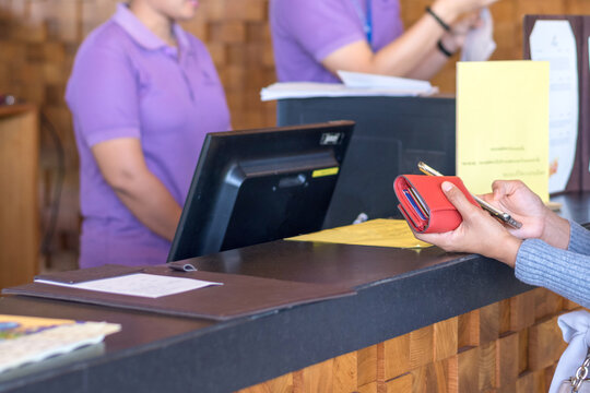 Hotel reception business concept. Customer holding purse and get information from mobile phone to checkin with receptionist working service at front desk lobby.