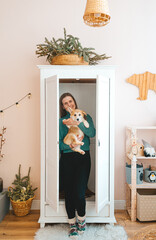 Beautiful girl with funny corgi puppy standing near big empty closet in the living room.