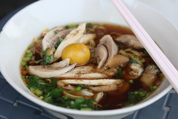 Thai style of chicken noodle with  boiled egg yolk in white bowl. One of the most popular Thai street food dishes to try.