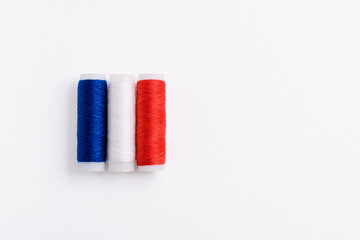 Three spools of thread for sewing are stacked in the form of the flag of France on a white background. Concept of French patriotism and the country's garment industry. There is a free empty space