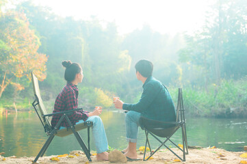 Happy traveler couple are enjoying with nature having coffee over lake in the morning , relaxation...