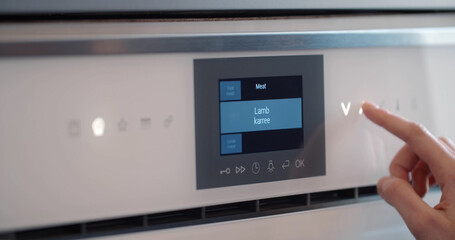 Woman hand control touch panel on electric oven in kitchen
