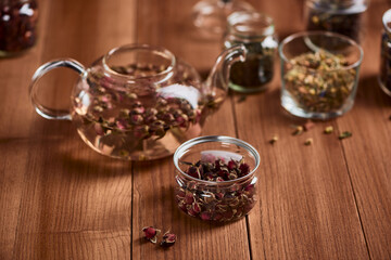 A jar of rose buds and a glass teapot on wooden table