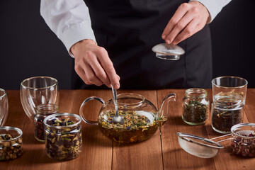 Barista brewing herbal tea in a glass teapot and stirring with a spoon