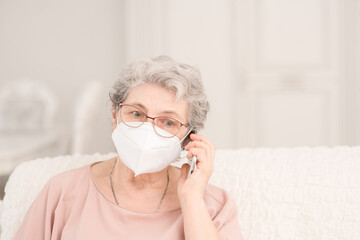 A pretty retired old woman with a medical mask during a coronavirus lockdown calls up with relatives via video chat using a phone. Quarantine during coronavirus pandemic concept