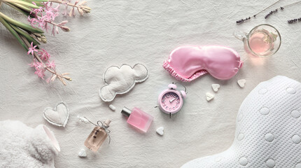Healthy night sleep concept. Off white, ivory textile flat lay. Pink hyacinth flower.Sleep mask, tea, glass,. Soft toys, clouds and heart. Fluffy bottle warmer, orthopedic pillow.