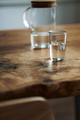 Stylish and cozy compositon of craft oak wooden table with chairs, watering can, glassy jug and modern floor in beautiful interior of design home. Template.