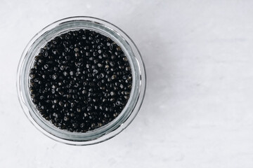 Fototapeta na wymiar Black caviar in glass jar on white stone background
