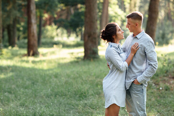 Fototapeta premium Cheerful young woman and man are hugging outdoors in summer park. Dating and romantic vacation. couple in love gently looking at each other on sunny day. Love and relationships between young people