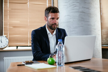 Young businessman using computer in his office. Handsome man working at his workplace..