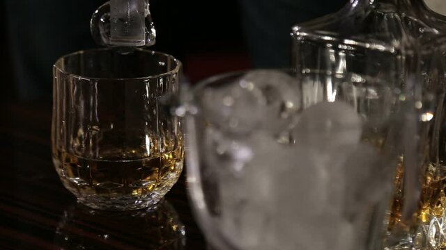 Closeup men hands putting ice cubes with forceps in glasses. Unknown men making drinks for party in restaurant. Man preparing whiskey for people in nightclub.