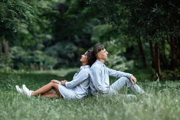 Outdoor shot of young happy couple in love sitting on grass on nature. Man and woman hugging, sunlight in summer park. Happy family in the evening sun light. The concept holiday.