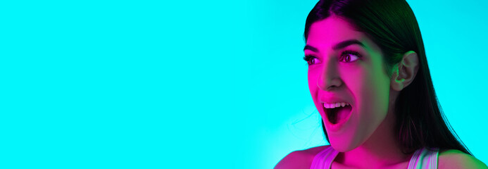Shocked. Close up brunette woman's portrait isolated on blue studio background in mixed neon light. Beautiful female model. Concept of human emotions, facial expression, sales, ad, fashion. Flyer.