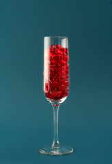 Beautiful card with champagne glass filled with transparent red hearts on dark aqua backdrop. Love and celebration concept. Great design for any purposes. Closeup.