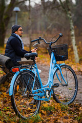 Fototapeta na wymiar Man sitter utomhus bredvid blå cykel och håller i en mobiltelefon