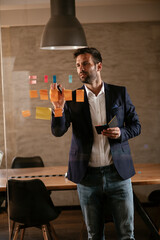 Businessman in conference room use sticky notes on glass wall. Handsome businessman making a business plan.