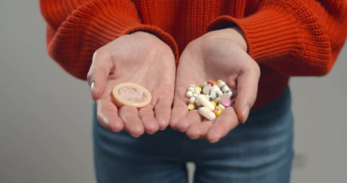 Close up of woman holding birth control pills and condom isolated on grey background