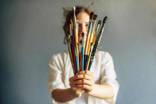 Horizontal of a candid female artist standing in her art studio with a lot of brushes in hands in focus.