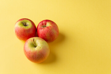 Three fresh red apples on a yellow background