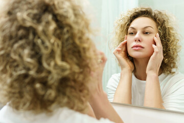 Woman with curly hair looking into the mirror in a bathroom