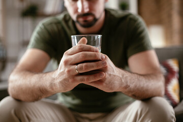 Close up of man`s hand holding a glass of whiskey. Lonely man is addicted of alcohol..