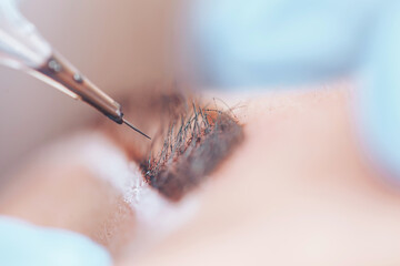beautician making a permanent make-up procedure on eyebrows using a machine, macro photo of needle - obrazy, fototapety, plakaty