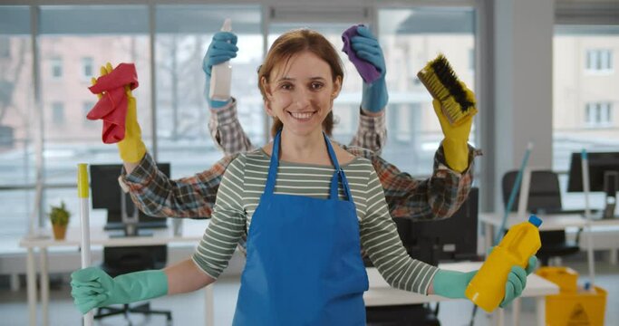 Multi-armed housemaid holding cleaning equipment and smiling at camera in office