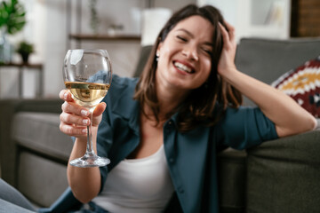 Beautiful woman sitting on the floor, drinking wine. Young woman celebrate with wine at home.