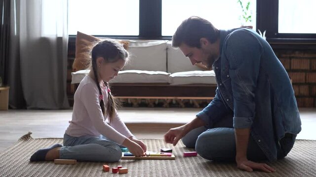 Happy parent dad helping daughter playing toys together on floor, having fun