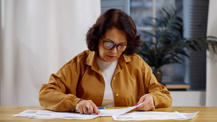 Senior mature business woman holding paper bill managing finances at home