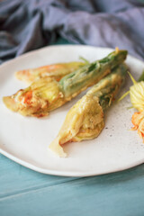 Battered and deep fried Courgette or Zucchini squash blossoms shot from above over a blue rustic table with blurred foreground and background.