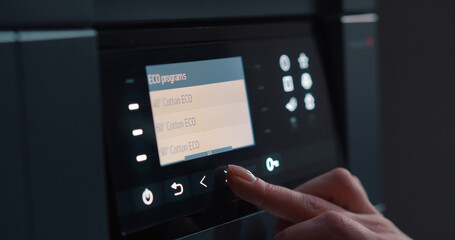 Close up of woman setting program on control panel of washing machine