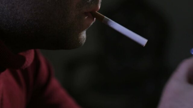 Man in the dark lights a cigarette with a match and starts smoking