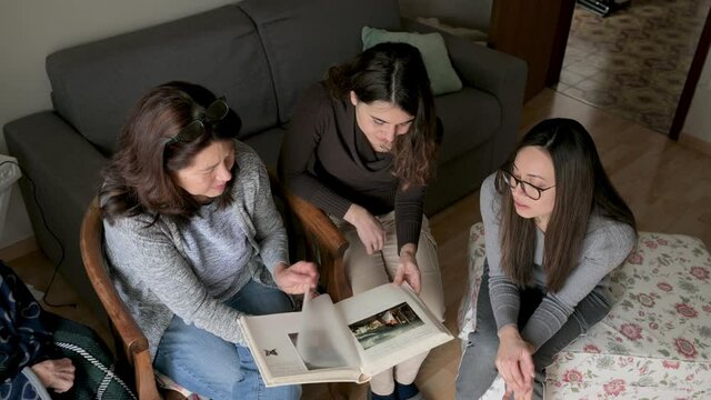 Positive females sitting in sofa looking a photo album. Mother, daughters, sisters with positive happy face. Memories, family concept.