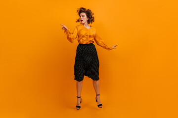 Enthusiastic girl posing in long skirt. Well-dressed lady jumping on yellow background.